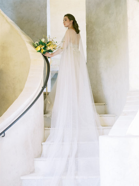 Bride wearing a wedding cape, walking up staircase.