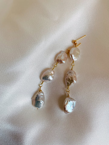 Close-up of Tia triple drop earrings on a silk background, showcasing the lustre of the pearls.
