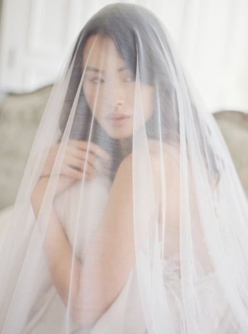 Close-up of a bride wearing the Angelique French silk drop veil over her face, showcasing the luxurious sheerness and incredible softness of the silk tulle.