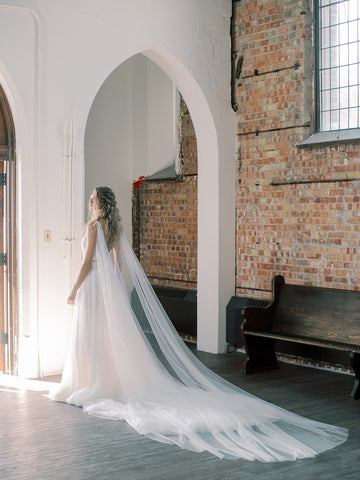 KAJA draped bridal cape veil styled with lace gown, photographed in an old church.