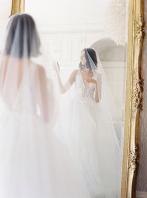 Close-up portrait of the bride smiling, standing indoors at Graydon Hall Manor. The AMELIE Veil blusher is draped softly over her face and shoulders, showcasing the tulle's sheer quality.