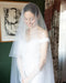 Close-up of a real bride smiling, wearing an off-the-shoulder gown. The AMELIE Veil blusher is pulled over her face, showcasing its sheer Italian illusion tulle.