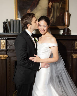 Real bride and groom portrait indoors near a dark wood fireplace. The bride wears the AMELIE Bridal Veil which is draped beautifully down her back.