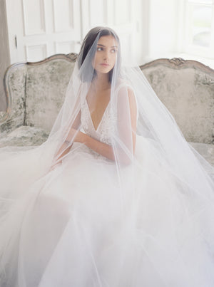 Close-up of a bride seated on a sofa in Graydon Hall Manor, wearing a tulle ballgown and the Amelie wedding veil over her face.
