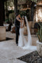 The bride and groom embrace in a semi-covered tropical courtyard. The Annabelle wedding veil flows behind the bride, pooling on the light stone floor.
