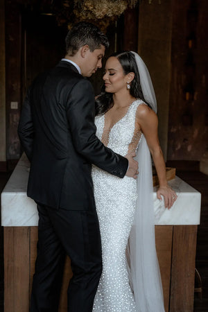 Romantic close-up of the bride and groom standing indoors. The sheer Annabelle English net veil rests over the bride's shoulder, highlighting her sparkling, fitted wedding gown.