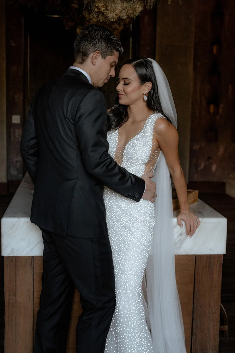Romantic close-up of the bride and groom standing indoors. The sheer Annabelle English net veil rests over the bride's shoulder, highlighting her sparkling, fitted wedding gown.