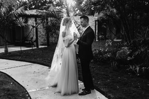 Bride wearing the ARIA sheer wedding veil with blusher with an off-the-shoulder wedding dress. She is holding hands with her groom.