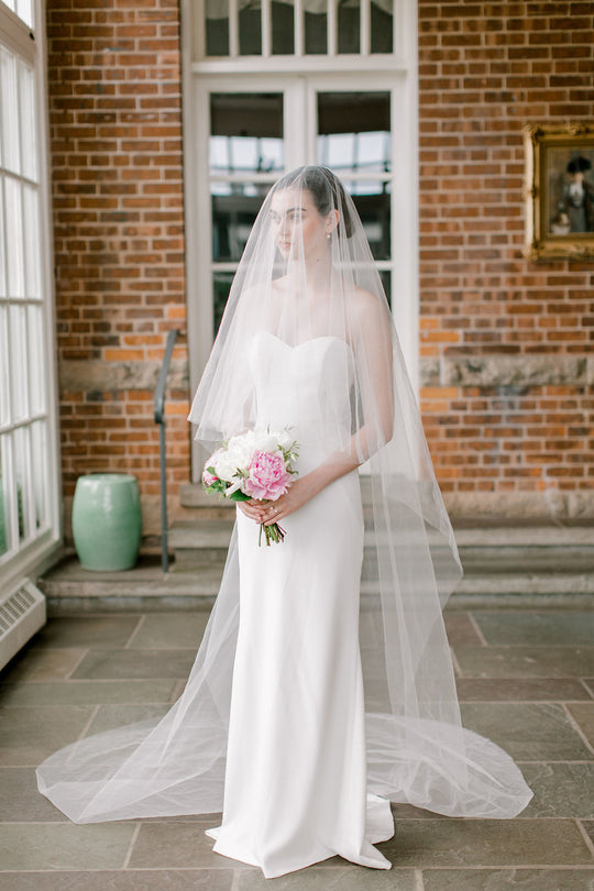 Sheer wedding veil with blusher. Bridal portrait with modern wedding dress and peony bouquet.