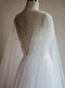 Close-up, rear view of the ARIELLE pearl bridal cape draped over a mannequin wearing a wedding gown. The sheer tulle is scattered with pearls, highlighting the deep V-back of the dress underneath.