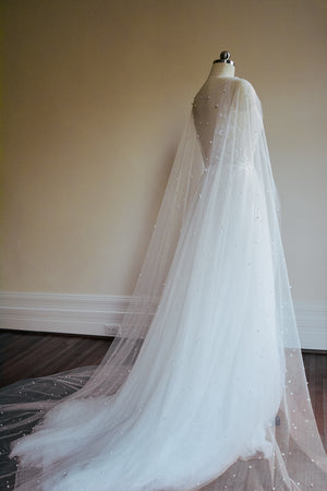 Full view of the ARIELLE pearl cape draped over a tulle bridal gown, demonstrating the sheer coverage across the shoulders and back.