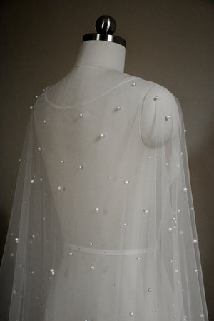 Close-up, angled shot of the back of the ARIELLE cape on a mannequin, highlighting the individual pearls on the sheer tulle across the shoulders and back.