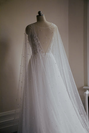 Close-up of the shoulder and back of the ARIELLE cape, highlighting the sheer tulle fabric and the density of the scattered pearls.