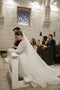 Bride wearing the Cassandra Veil with the long blusher pulled back and open, creating a voluminous two-tier silhouette. The sheer Italian tulle train cascades behind her as she kneels during the ceremony.
