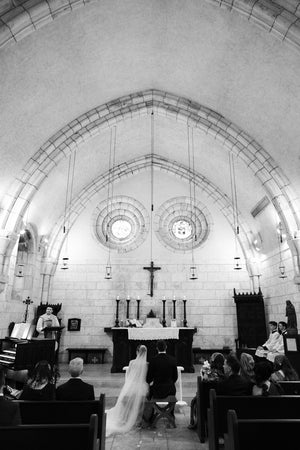 High-angle view of the Cassandra veil's sheer tulle train pooling on the altar floor as the bride and groom listen to the priest during the wedding ceremony.
