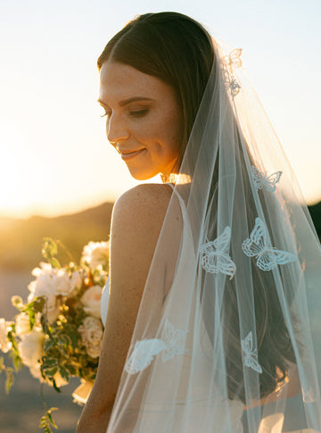 A close-up, rear view of a bride wearing the Dream butterfly veil styled with hair down, showcasing the density of the butterfly appliques scattered over the sheer illusion tulle.