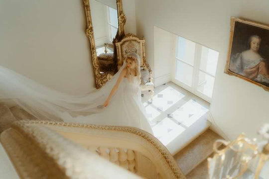 Bride walking down chateau staircase with silk wedding veil trailing behind her.