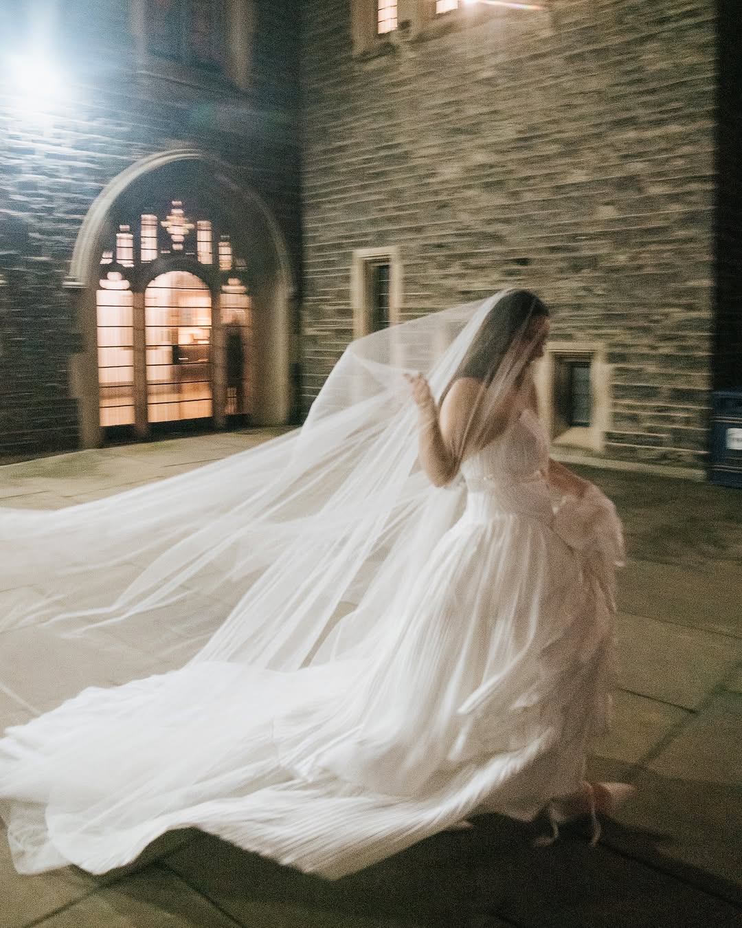 Woman in a white wedding dress and a long silk wedding veil standing in an old stone church.