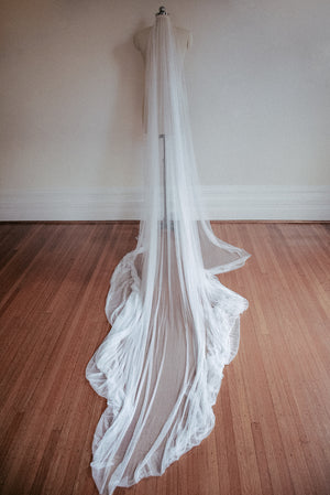 The Isabelle silk veil styled on a dress mannequin, with the train of the veil softly pooling on the ground to show the softness and fluidity of the silk tulle.