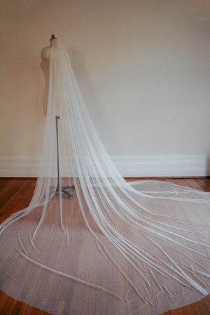 The Isabelle silk wedding veil shown on a dress mannequin, with the extra wide train of the veil fanned out on the floor.