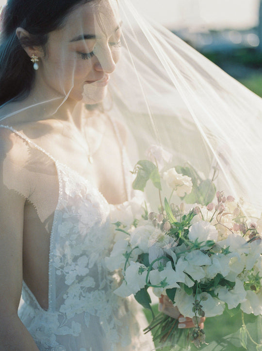 Bride wearing a wedding veil over her face and holding a white bouquet.