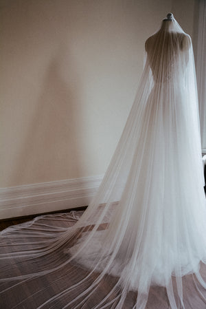 The Monique silk wedding veil shown on a dress mannequin wearing a bridal gown. The wide veil train is fanned out on the ground behind the dress. 