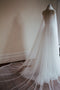 The Monique silk wedding veil shown on a dress mannequin wearing a bridal gown. The wide veil train is fanned out on the ground behind the dress. 