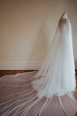 The Monique silk wedding veil with blusher shown from the side. The veil is draped over a dress mannequin, with the dramatic wide train fanned out on the floor.