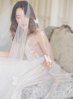 A bride wearing the REVERIE wedding veil with butterflies and lace wedding dress.