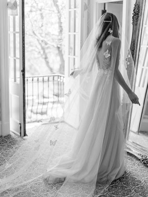 A bride wearing the REVERIE wedding veil with butterflies and lace wedding dress; she is standing in front of the mirror in the Graydon Hall bridal suite. 