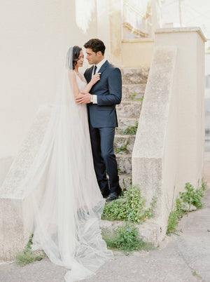 Bride standing on stairs with the Talitha single-tier veil spread out on the steps behind her.
