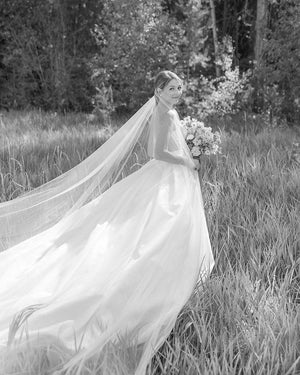 Portrait of the bride holding her bouquet with the sheer, long Talitha wedding veil flowing behind her.