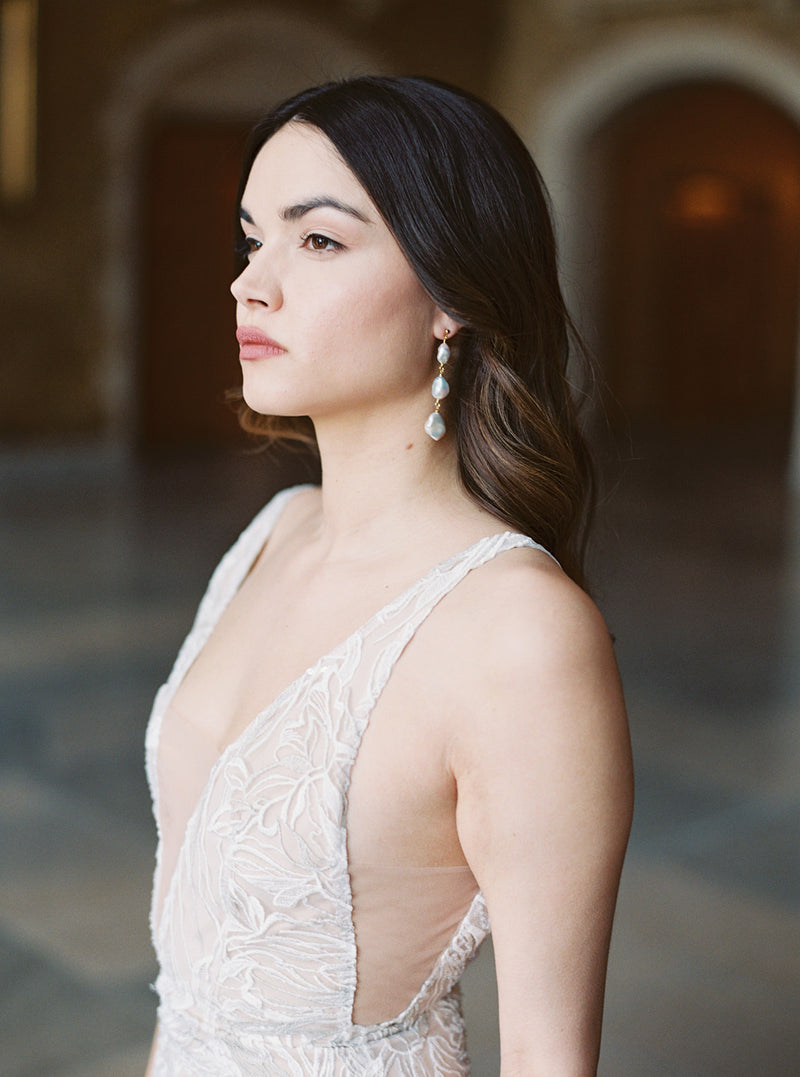Profile shot of bride wearing Tia triple drop baroque pearl earrings, which highlight the length of the neck and open neckline of the lace dress.