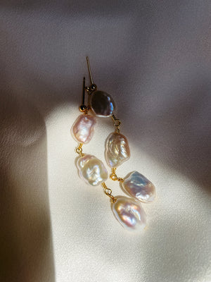 Detail shot of Tia long drop earrings, highlighting the unique, iridescent freshwater pearls and delicate wire wrapping on a soft lit background.