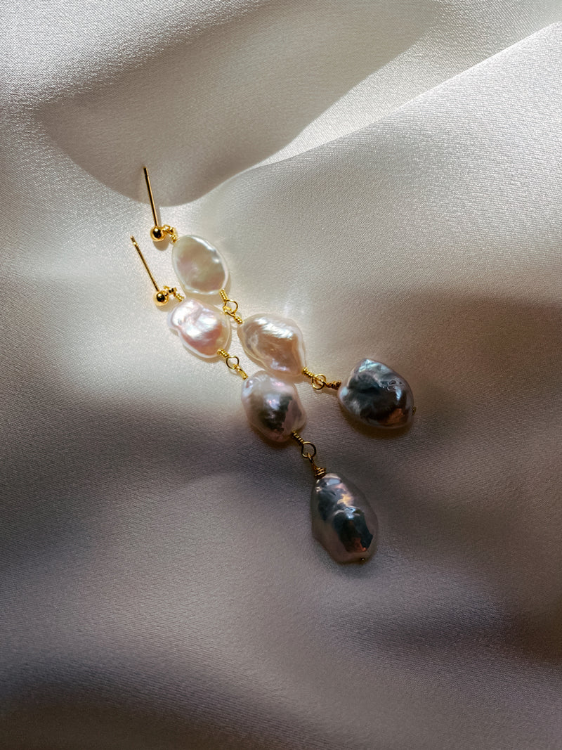 Tia triple drop earrings with baroque freshwater pearls in a cascading design, lying on silk.