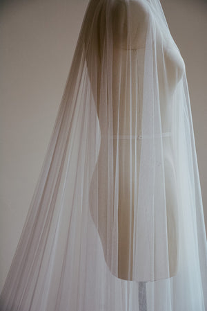 A close-up detail shot of a sheer Juliet cap wedding veil on a mannequin, highlighting the drape of the delicate French silk tulle as it falls gracefully past the waist
