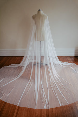 A full back view of a bridal mannequin wearing the Lilybeth Juliet cap wedding veil. The sheer French silk tulle cascades smoothly down the back, fanning out into an extra-wide, dramatic train on the floor.