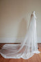 A side profile of a bridal mannequin wearing a silk Juliet cap wedding veil. The buttery-soft French silk tulle drapes fluidly down the body, softly pulling back to pool into a romantic train on the floor behind it.   