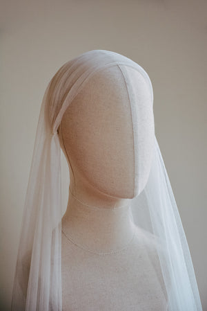 A front view of a bridal mannequin wearing the Lilybeth silk Juliet cap wedding veil with the blusher flipped back. The delicate French silk tulle smoothly hugs the crown of the head and cascades softly down the sides, covering the shoulders.