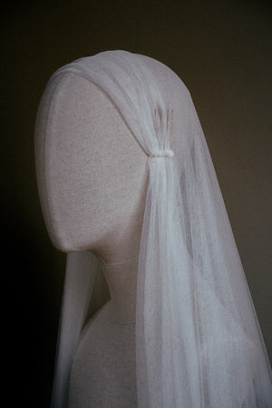 A close-up side view of the Lilybeth Juliet cap veil on a mannequin, highlighting the delicate hand-sewn gathering and the small metal comb used to securely anchor the silk tulle to the hair.