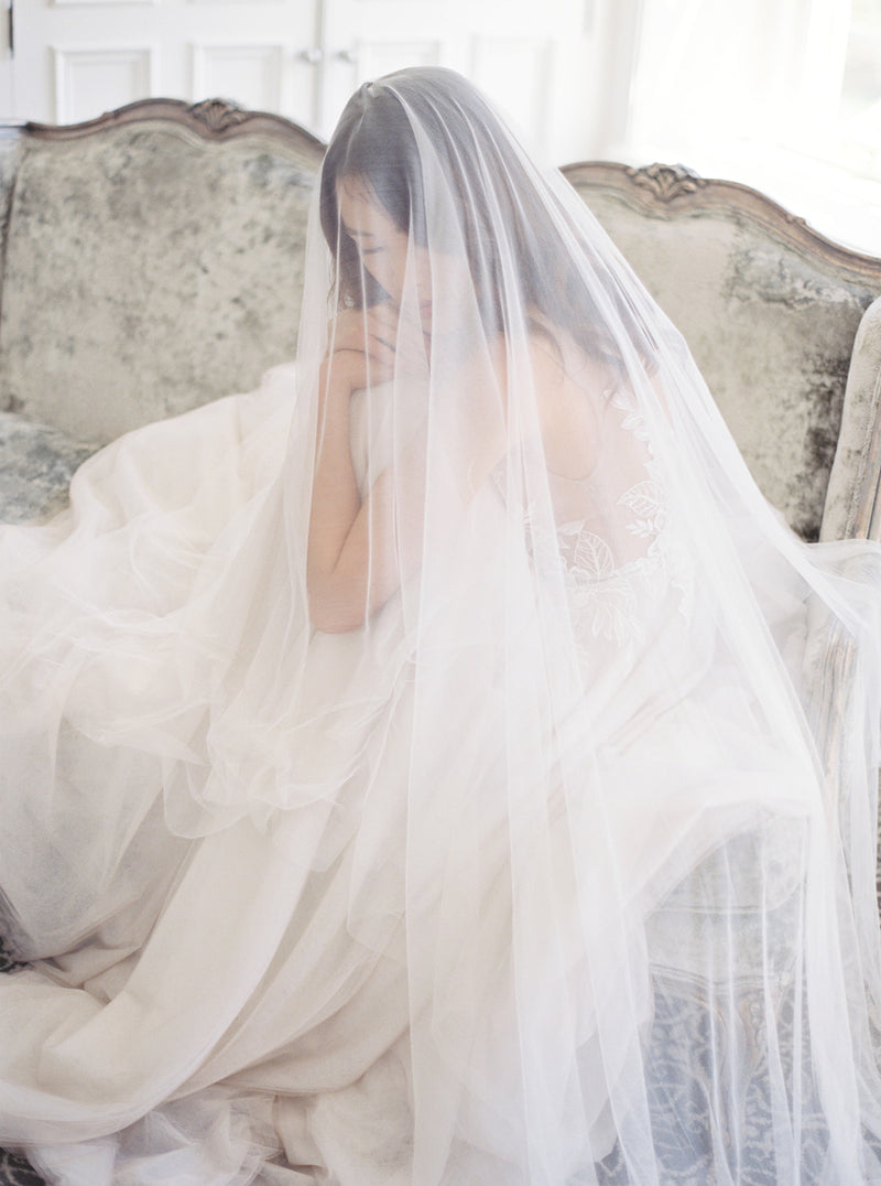 Close-up of the bride seated in the bridal suite at Graydon Hall Manor. The sheer Angelique Silk Drop Veil drapes gently over her face and shoulders, highlighting the softness of the French silk tulle.