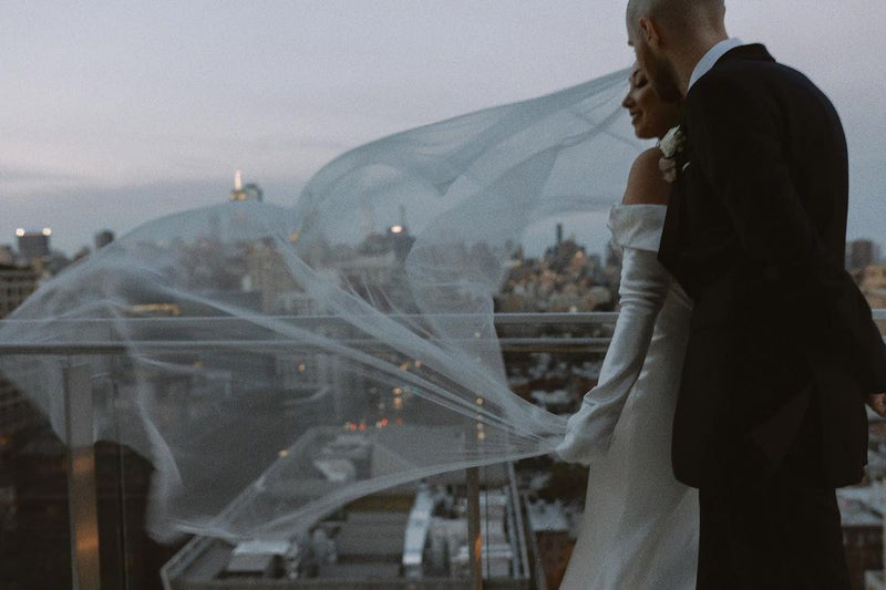 A romantic rooftop photo of the bride and groom at dusk. The soft Angelique French silk veil catches the wind, showcasing the beautiful movement of the silk tulle. 