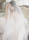A veiled bride touches her hair while seated on an antique sofa in Graydon Hall Manor. The fluid Angelique French Silk Veil completely surrounds her in a soft layer. 