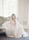Romantic portrait of a bride in the light-filled Graydon Hall Manor bridal suite. She is veiled with the soft Angelique French Silk Drop Veil, seated on a velvet-covered chaise lounge.