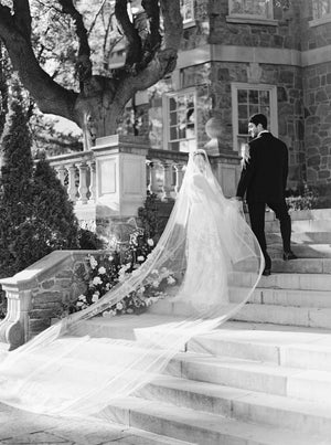 Black and white fine art photo at Graydon Hall of the Cassandra Long Blusher Veil sweeping down the grand stone staircase. The sheer Italian tulle train dramatically trails behind the bride.