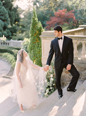 Romantic fine art photo at Graydon Hall of the Cassandra Veil. The bride, wearing a gold leaf headpiece, looks up at the groom as they stand together on the grand stone staircase.