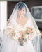 Real bride portrait wearing the Cassandra Veil's sheer long blusher draped over her face. The fine Italian tulle creates a beautiful, soft layer over the bride holding her warm-toned wedding bouquet.