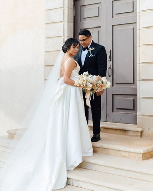 Real bride wearing the Cassandra Long Blusher Veil with the blusher open. The sheer Italian tulle creates a soft two-tier look, complementing the bride's elegant gown with a large back bow.