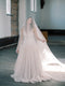 Full body shot of the bride standing in a high-ceiling church with high windows, with the Grace silk blusher veil covering her face and trailing dramatically behind her.