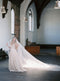 Wide shot of the bride standing alone in a large, bright church, showing the full, dramatic length of the Grace silk wedding veil train laid out.